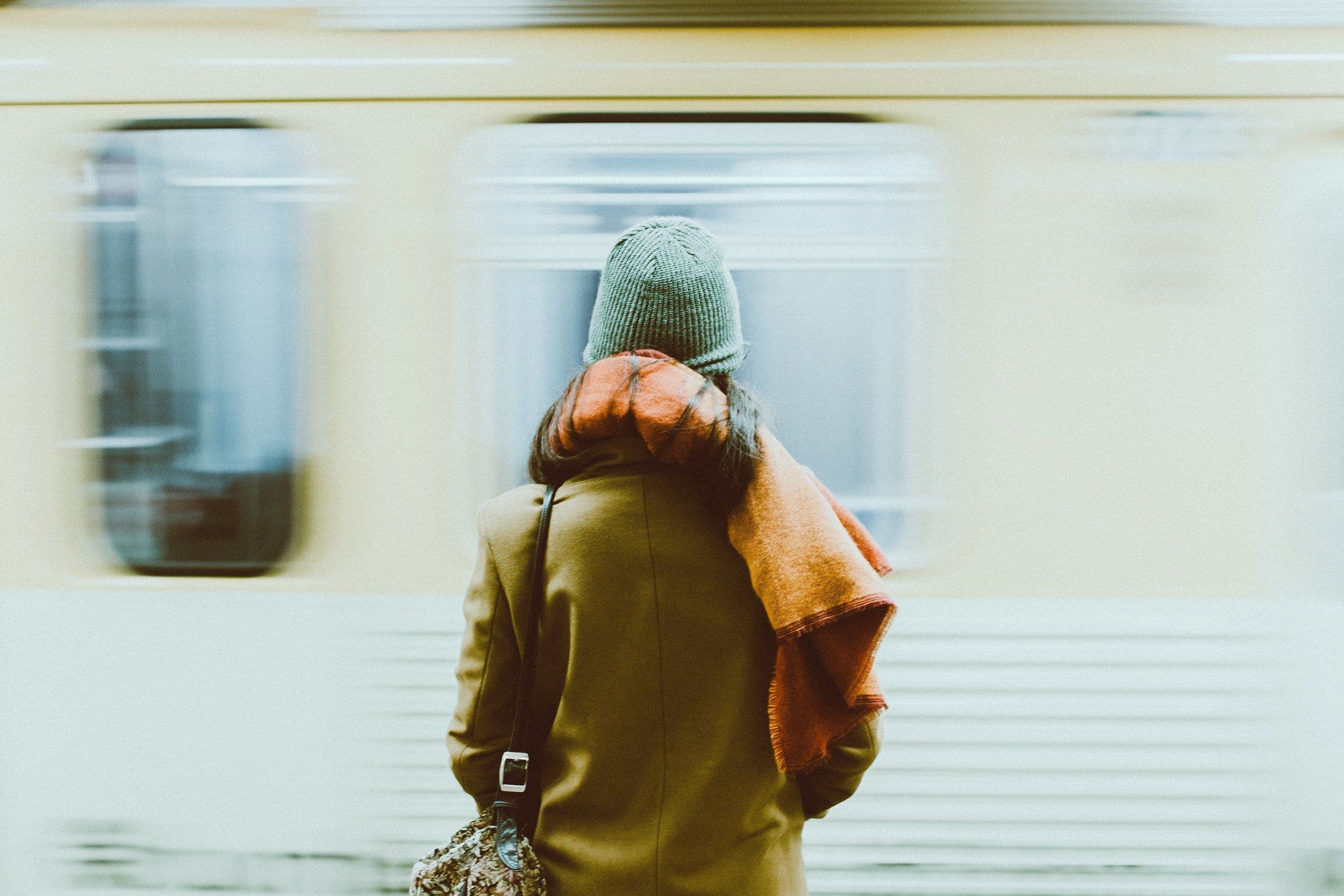 a person standing in front of a moving train wearing a scarf
